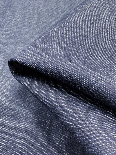 Close-up of the Stretch Denim - Black Iris - 140cm fabric with a folded corner, highlighting its texture and weave pattern. Made by Super Cheap Fabrics from ring-spun cotton, the dense, slightly shiny threads create a subtle diagonal design typical of this durable material.