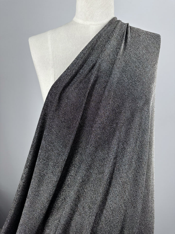 The Metallic Lycra - Silver fabric from Super Cheap Fabrics is elegantly draped over a white mannequin against a neutral background. The textured surface of this 160cm wide gray fabric shines beautifully, making it an ideal choice for crafting sophisticated tops or dresses.