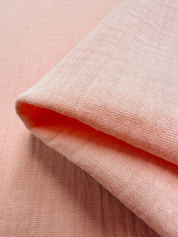 Close-up of the Super Cheap Fabrics Muslin in Peach Parfait, measuring 135cm wide and crafted with a textured finish. The reusable cloth showcases a subtle weave pattern, contributing to its soft and slightly sheer appearance. The background matches in color, achieving a monochromatic look.