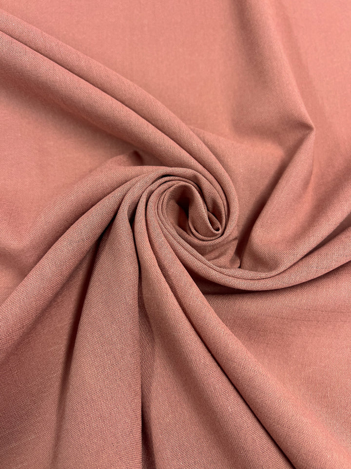 A close-up image of a piece of the Linen Blend - Muted Clay - 145cm fabric from Super Cheap Fabrics, artfully twisted into a spiral pattern at its center. The lightweight linen blend appears to be soft and smooth, with a gentle texture and subtle sheen, perfect for clothing and upholstery projects.