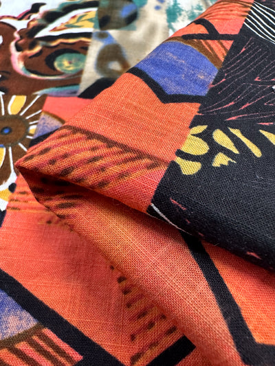 A close-up showcases vibrant, layered fabrics featuring orange, black, and blue geometric shapes with floral and abstract patterns on the breathable Super Cheap Fabrics' Linen Blend - Patch - 145cm. The detailed textures and folds add to its vibrancy.