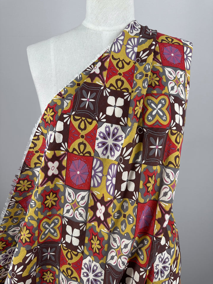 A mannequin draped with Super Cheap Fabrics' Linen Blend - Mosaic - 145cm showcases a vibrant and lightweight linen fabric. This breathable design features geometric and floral patterns, including squares and stars, in shades of red, yellow, brown, and purple.