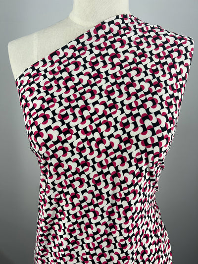 The dress mannequin showcases a "Mirrors" one-shoulder garment made from Super Cheap Fabrics' medium-weight Printed Lycra, featuring a geometric pattern with interlocking black, pink, and white shapes on a light background. Width: 150cm.