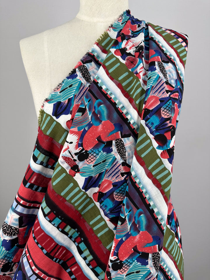 A mannequin adorned with the Linen Blend - Mapalo - 145cm from Super Cheap Fabrics displays a vibrant abstract design featuring colorful stripes, geometric shapes, and patterns in hues of red, green, blue, and black. The lightweight fabric gracefully envelops the mannequin's shoulders in a loose embrace.