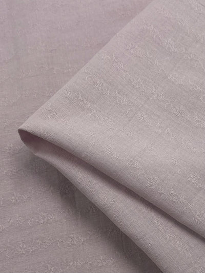 The "Textured Cotton - Burnish Lilac - 145cm" from Super Cheap Fabrics features a folded fabric in a light lavender hue with a gentle, textured pattern. Crafted from 100% cotton, its surface is smooth and ultra-lightweight, showcasing intricate detailing for an elegant appearance.