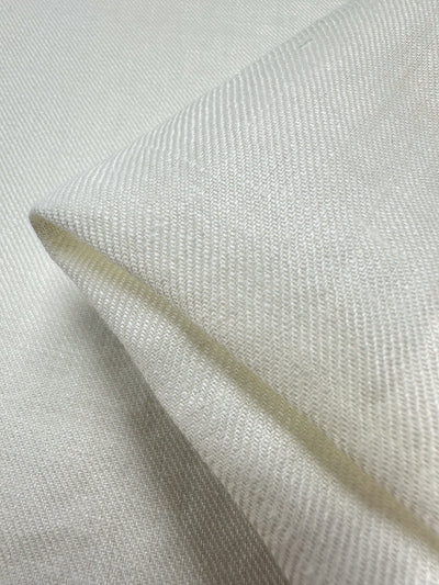 Close-up of a Pure Washed Linen - Lucent White by Super Cheap Fabrics, featuring a textured pure linen fabric folded at the corner, beautifully showcasing its intricate weave pattern. The light accentuates the subtle lines and texture, creating a soft and smooth appearance with its lightweight elegance.