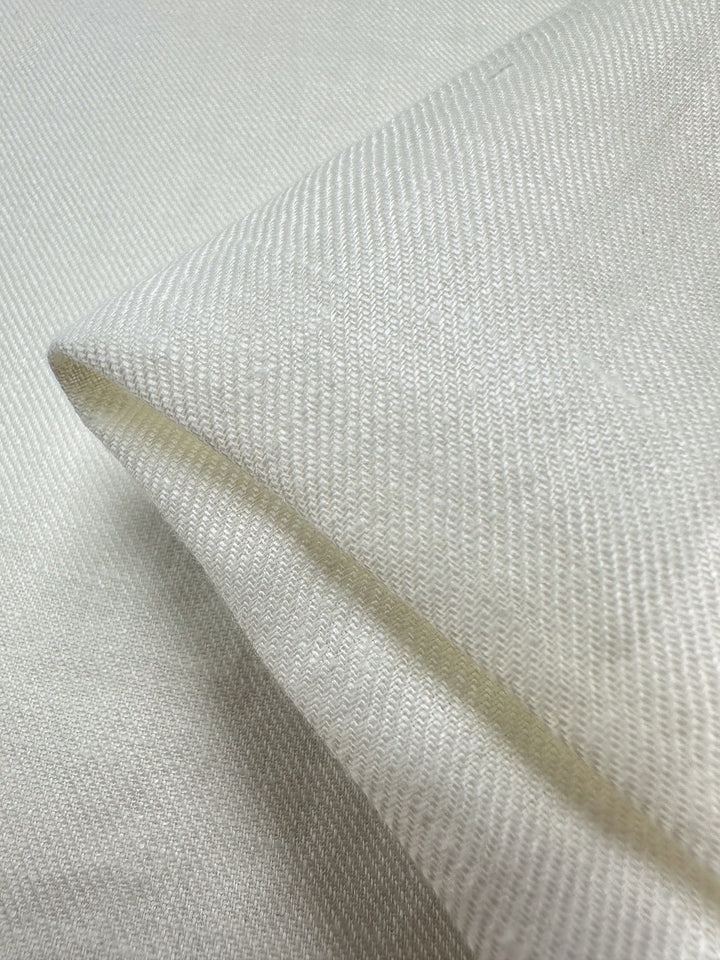 Close-up of a Pure Washed Linen - Lucent White by Super Cheap Fabrics, featuring a textured pure linen fabric folded at the corner, beautifully showcasing its intricate weave pattern. The light accentuates the subtle lines and texture, creating a soft and smooth appearance with its lightweight elegance.