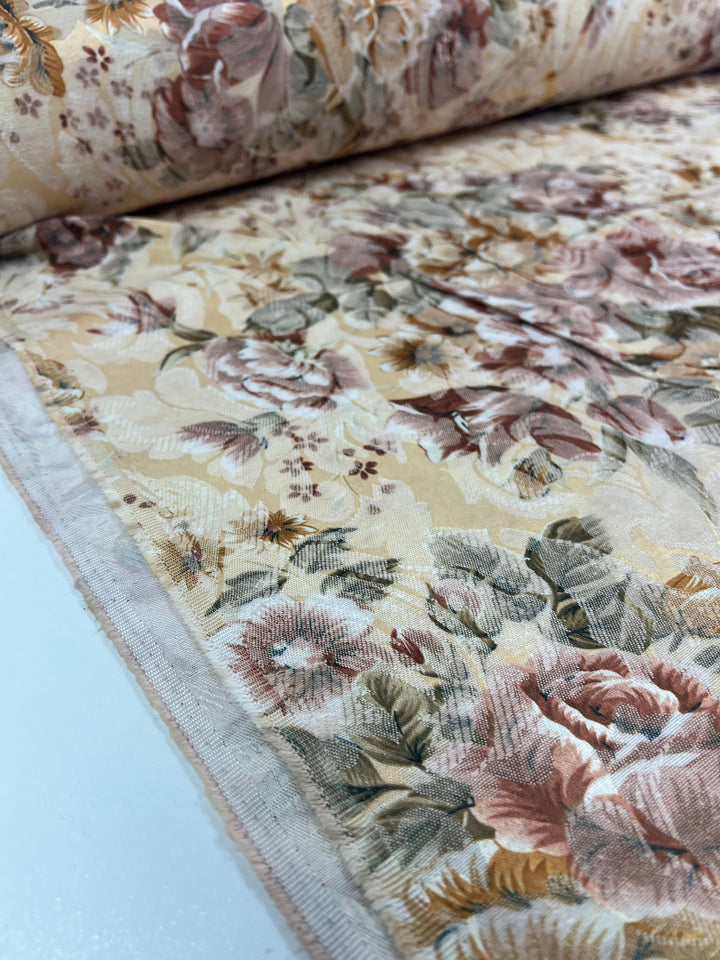 A roll of Designer Brocade - Vintage - 150cm from Super Cheap Fabrics showcases a medium-weight floral-patterned fabric in pink, green, and beige hues. This fabric highlights a stunning display of intricate Italian designs featuring flowers and leaves against a light background.