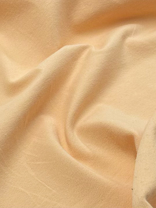 A close-up of Super Cheap Fabrics' Cotton Lycra in Caramel Cream, measuring 165cm, reveals gentle folds and creases for a textured look. The soft, breathable fabric reflects light smoothly across its surface like caramel cream.