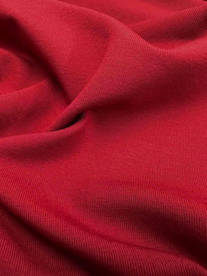 A close-up of Super Cheap Fabrics' Karanda Red Cotton Lycra, 165cm wide, displays its textured surface with gentle folds. The medium-heavy weight fabric appears soft and slightly ribbed, indicating a possible woven or knitted composition.