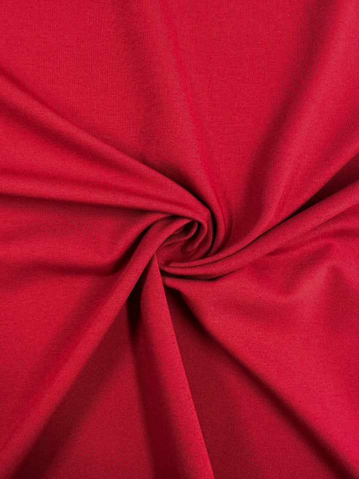 A close-up of Super Cheap Fabrics' Cotton Lycra - Karanda Red - 165cm reveals a spiral pattern on the medium-heavy cotton lycra. The smooth surface with shadows and highlights enhances the texture and depth of its folds.