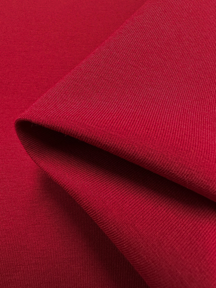 A close-up of folded Cotton Lycra - Karanda Red by Super Cheap Fabrics showcases its smooth, woven texture. Light enhances the rich color and fine details of this medium-heavy 165cm fabric.