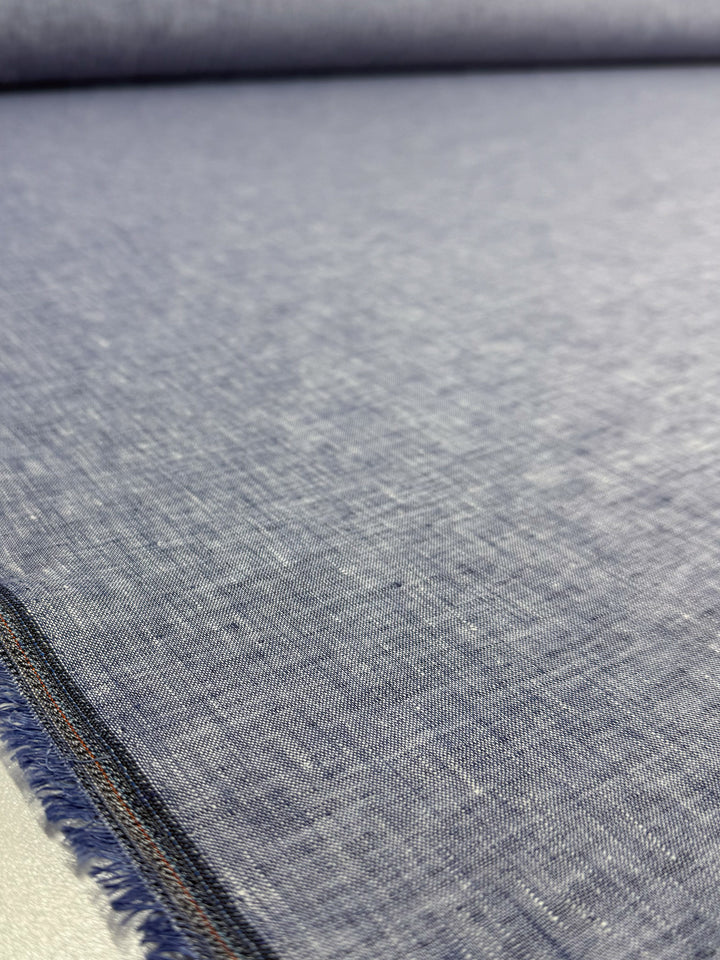Close-up of Super Cheap Fabrics’ Pure Linen - Indigo Husk (135cm), showing its lightweight chambray texture, subtle heathered look, and visible selvage edge with fine threads.