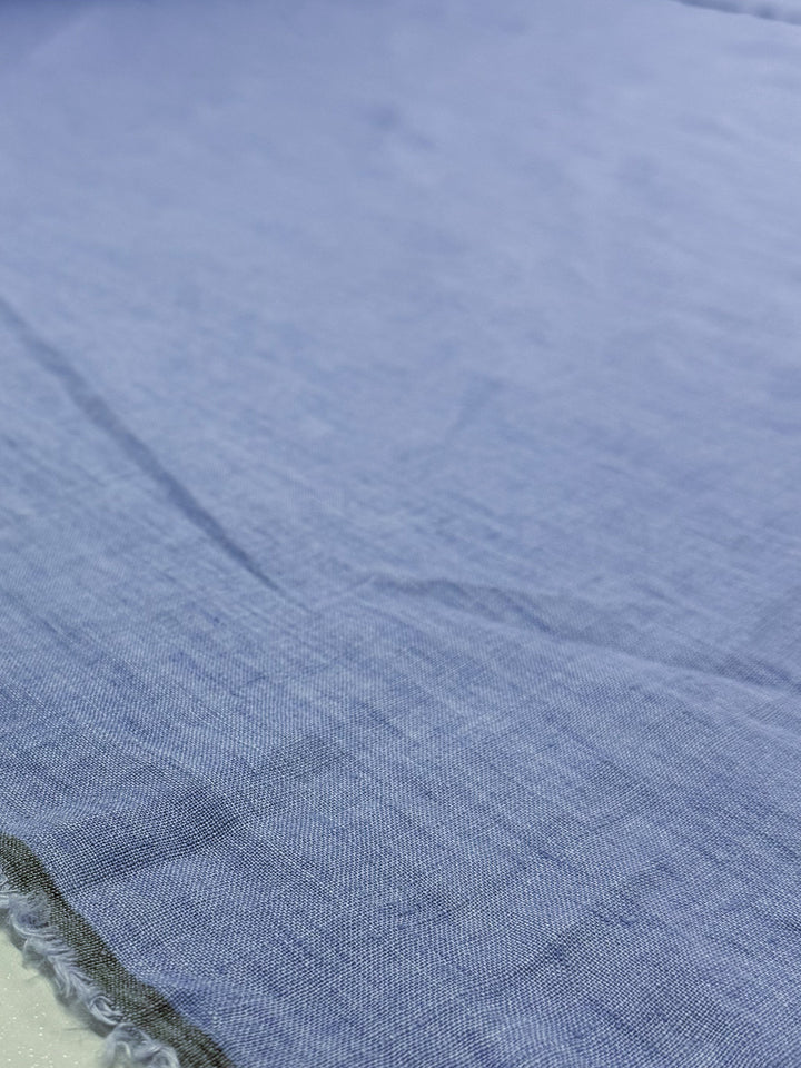 A close-up of Pure Linen - Washed Sky by Super Cheap Fabrics (142cm wide) reveals its light blue, slightly wrinkled texture and visible edge seam, highlighting its light to medium weight.