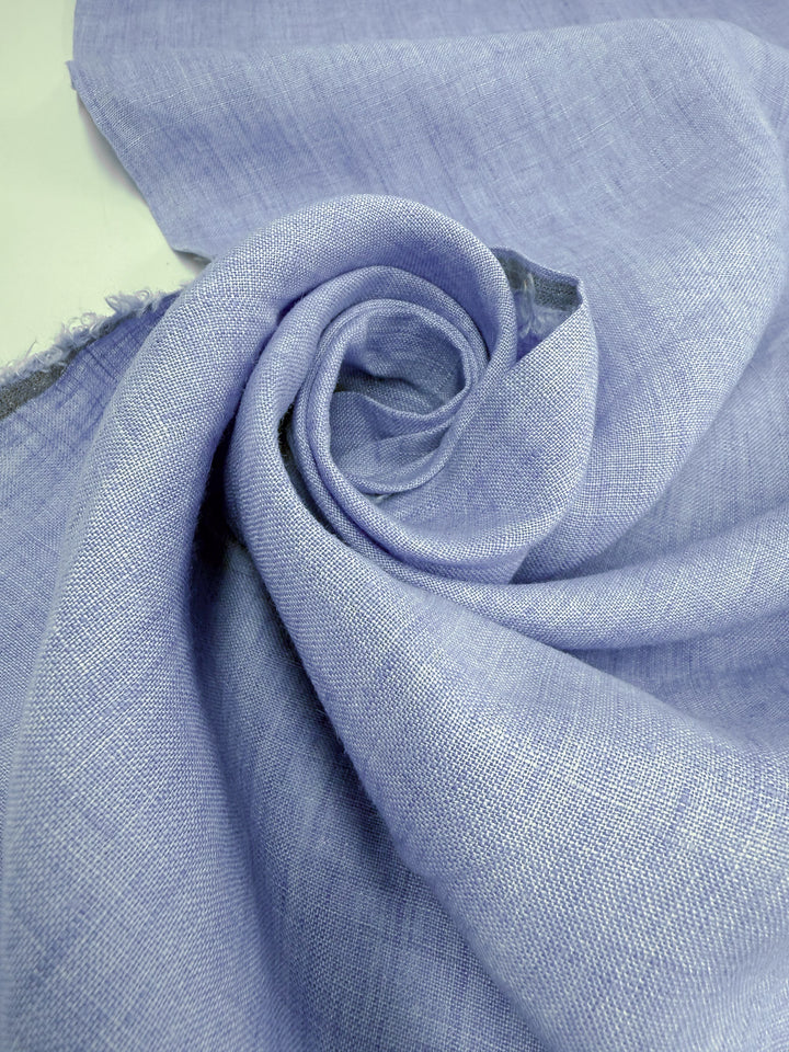 A close-up shows the soft texture and fine weave of Super Cheap Fabrics’ Pure Linen - Washed Sky (142cm), loosely rolled in a spiral.