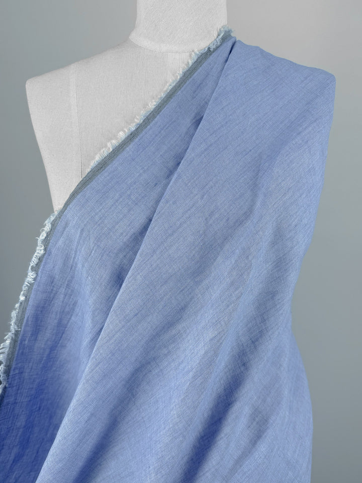 Super Cheap Fabrics' Pure Linen - Washed Sky (142cm) features light blue, textured linen with frayed edges, shown draped over a white dress form against a neutral background.