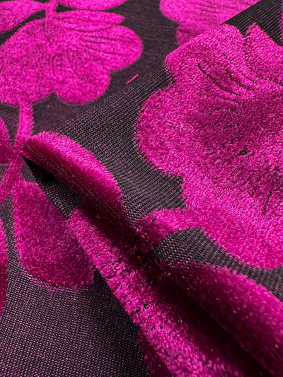 Close-up of Super Cheap Fabrics' Burnout Velvet - Cactus Flower. This luxurious 160cm fabric features bright fuchsia floral patterns on a dark background, with a soft and velvety texture. The flowers stand out against the subtle mesh, with slight folds highlighting its sophisticated style.