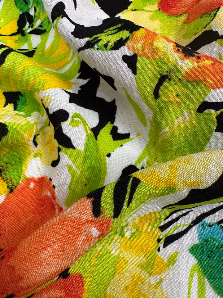 A close-up of Super Cheap Fabrics' Linen Blend - Black Forest (145cm) reveals a vibrant floral pattern in orange, yellow, green, and black on white, creating an abstract, colorful look with visible folds and texture—ideal for versatile home decor.