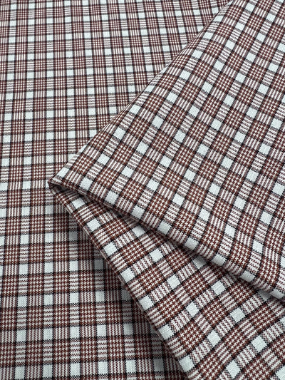 A close-up of Super Cheap Fabrics' Shirting - Terra reveals a folded polyester cotton cloth with a 147cm width in a red and white checkered pattern. The layered, lightweight fabric showcases a detailed grid design with hints of terracotta shades.