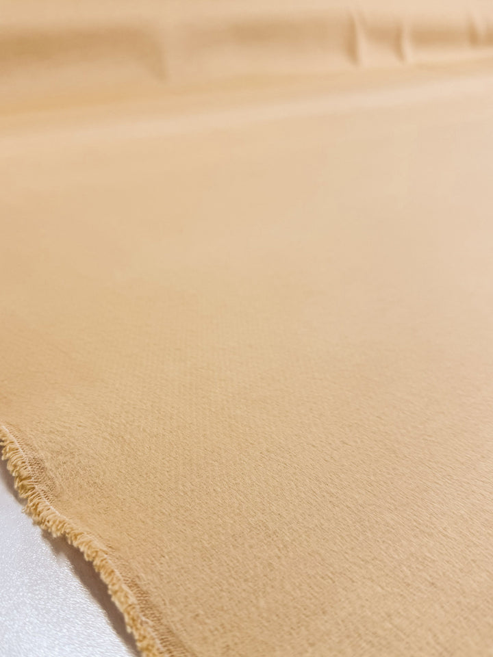 A close-up of Super Cheap Fabrics’ Wool Cashmere - Banana Crepe (150cm) in beige, laid flat to reveal a slightly frayed edge left and a smooth, subtly textured surface.