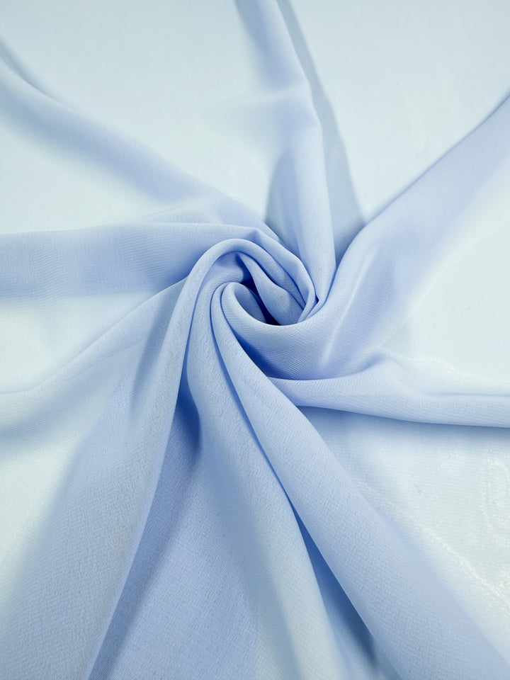The Hi-Multi Chiffon - Windsurfer - 150cm from Super Cheap Fabrics is a light blue sheer fabric, artfully spiraled to create soft folds and highlight its delicate, lightweight texture on a smooth surface.