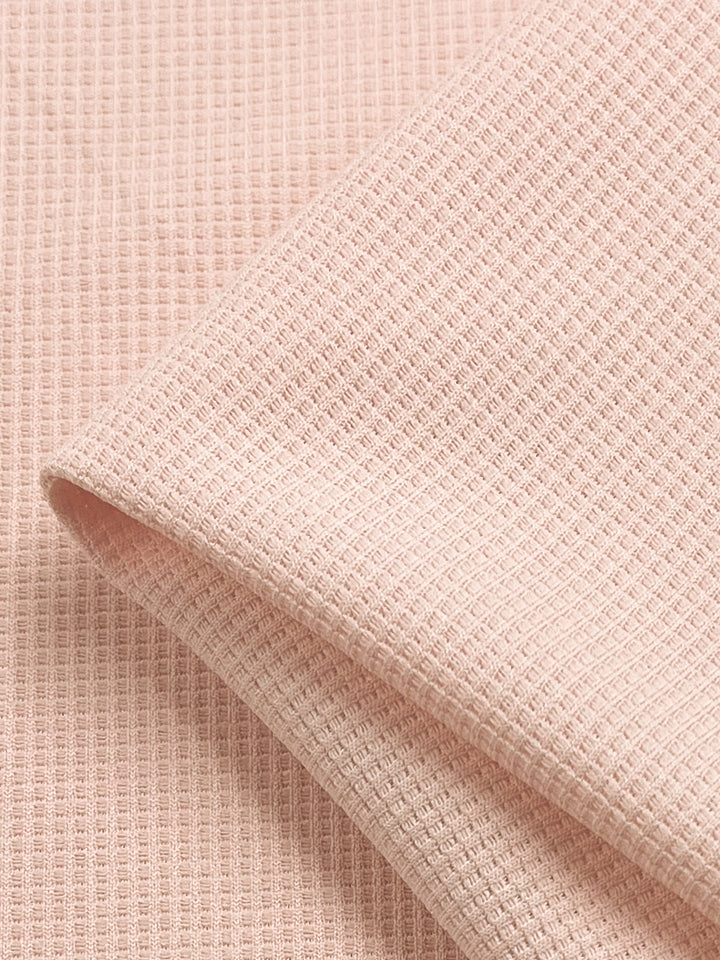 A close-up of the Waffle Knit fabric from Super Cheap Fabrics in Pearl Blush reveals its intricately textured grid pattern. The light beige material, measuring 170 cm wide, is neatly folded, highlighting its woven structure and three-dimensional appearance.