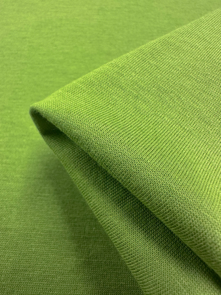 An up-close look at the Cotton Jersey - Titanite by Super Cheap Fabrics reveals its textured surface and green shades from lighting and layers. This 160cm cotton fabric appears soft and smooth, perfect for clothing or upholstery.