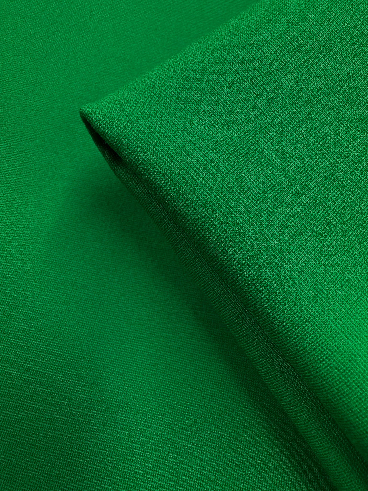 A close-up of Super Cheap Fabrics' Milano Ponte - Jolly Green (160cm) reveals its smooth, heavy-weight, woven texture and vibrant solid color with a neatly folded edge.