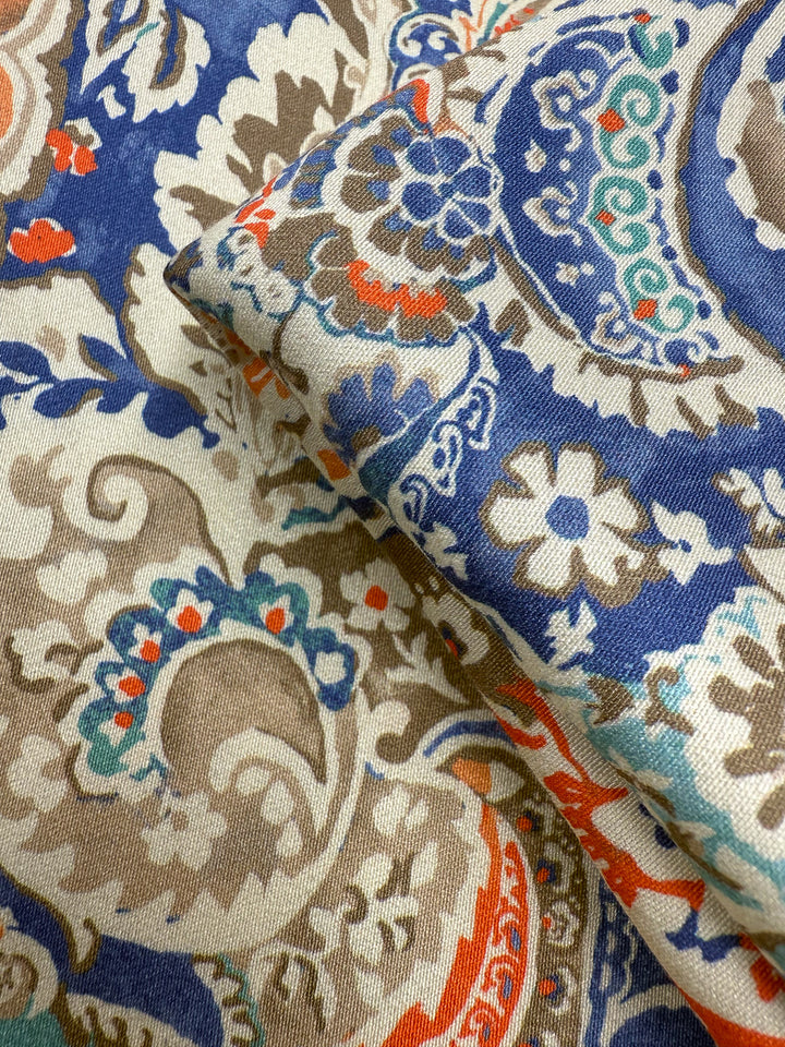 Super Cheap Fabrics' Mercerised Rayon - Paisley Fusion - 150cm features a lightweight rayon with detailed blue, brown, orange, and cream paisley patterns, including floral and ornamental motifs on a textured surface.