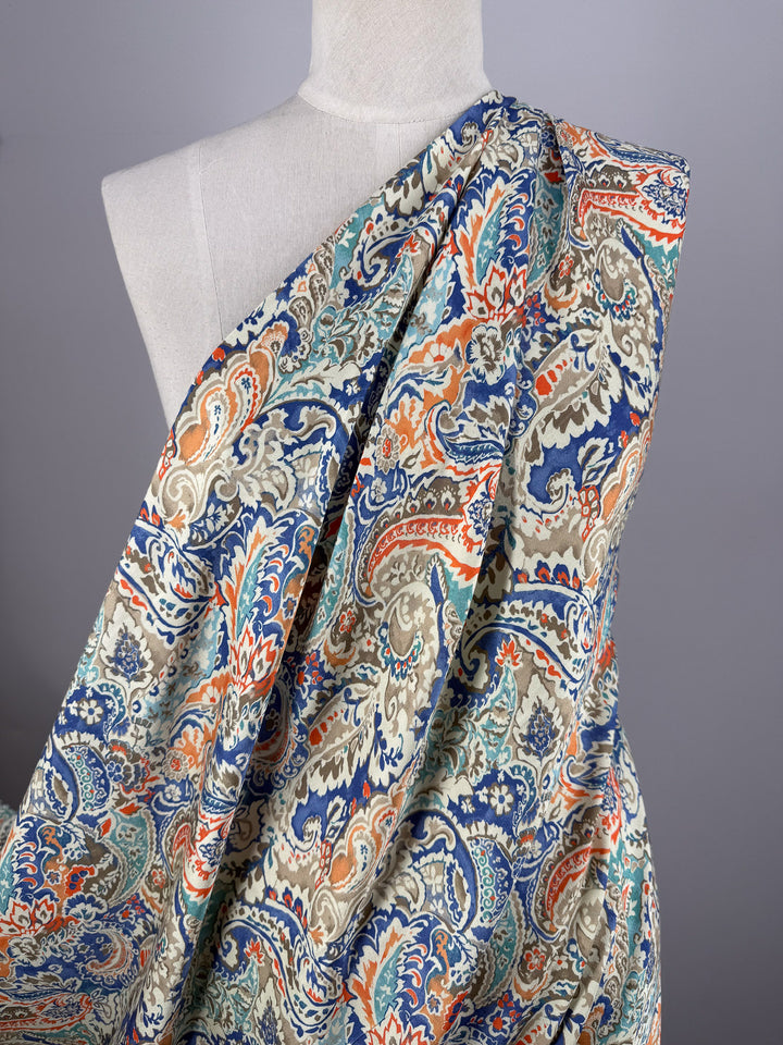 A mannequin displays Super Cheap Fabrics’ Mercerised Rayon - Paisley Fusion (150cm), a lightweight rayon fabric featuring an intricate paisley pattern in blue, orange, beige, and green on a neutral background.