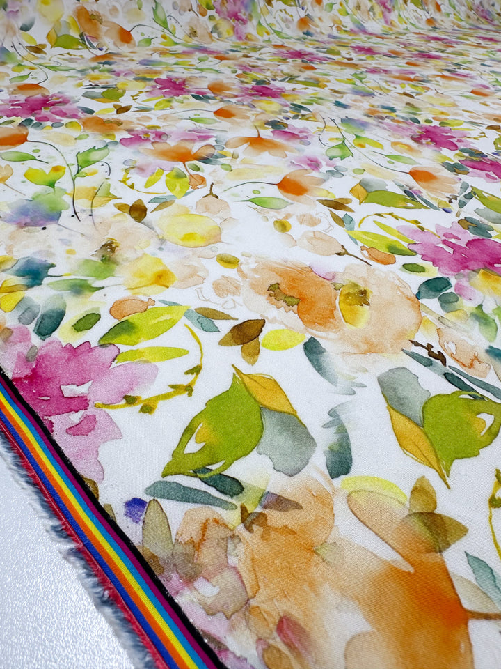 Super Cheap Fabrics presents the Designer Rayon - Jesse (145cm), a versatile fabric with vibrant watercolor-style floral prints in pink, orange, yellow, and green. Enhanced by a multicolored striped border, it’s perfect for any project needing a colorful touch.