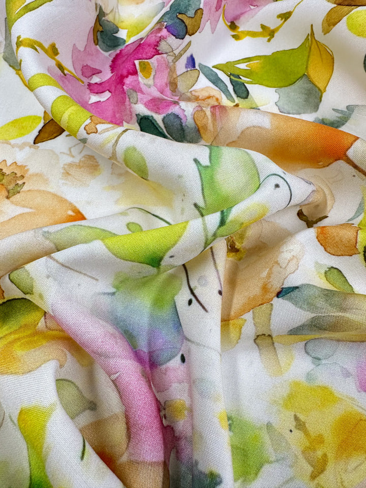 Close-up of Designer Rayon - Jesse by Super Cheap Fabrics: a 145cm fabric featuring a colorful floral pattern with a mix of green, pink, yellow, and orange watercolor-style flowers. Its vibrant prints softly drape, creating gentle folds and shadows.