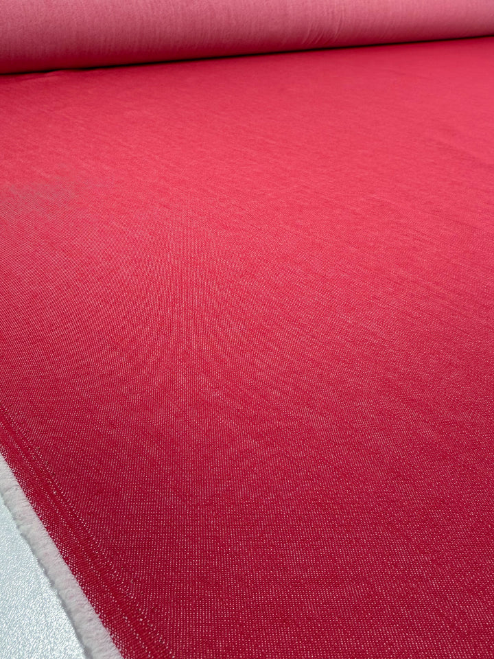 A close-up of Super Cheap Fabrics' Denim - Hibiscus - 150cm shows the fabric's smooth, even texture and vibrant red color, spread flat to highlight its quality.