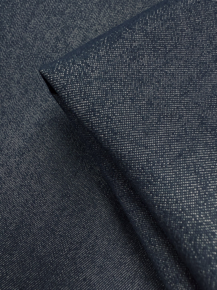 Close-up of Super Cheap Fabrics' Denim - Classic - 150cm: folded dark blue, medium-weight fabric with a subtle textured pattern and tiny white flecks for a slightly speckled look.