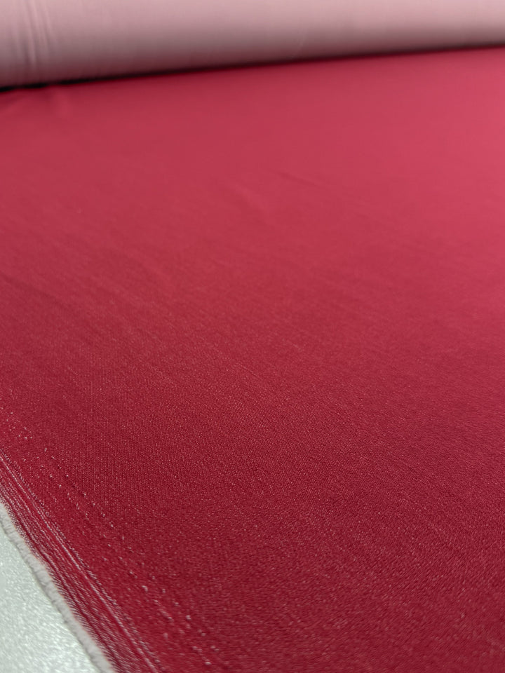 A close-up of Stretch Denim - Scooter Red (147cm) by Super Cheap Fabrics shows its smooth texture and vibrant, even red color as the fabric is neatly spread out.
