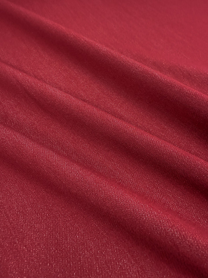 Stretch Denim - Scooter Red by Super Cheap Fabrics is a red fabric with a soft, smooth texture and subtle sheen. Its horizontal folds create gentle shadows, giving the 147cm wide material a slightly reflective and stylish appearance.