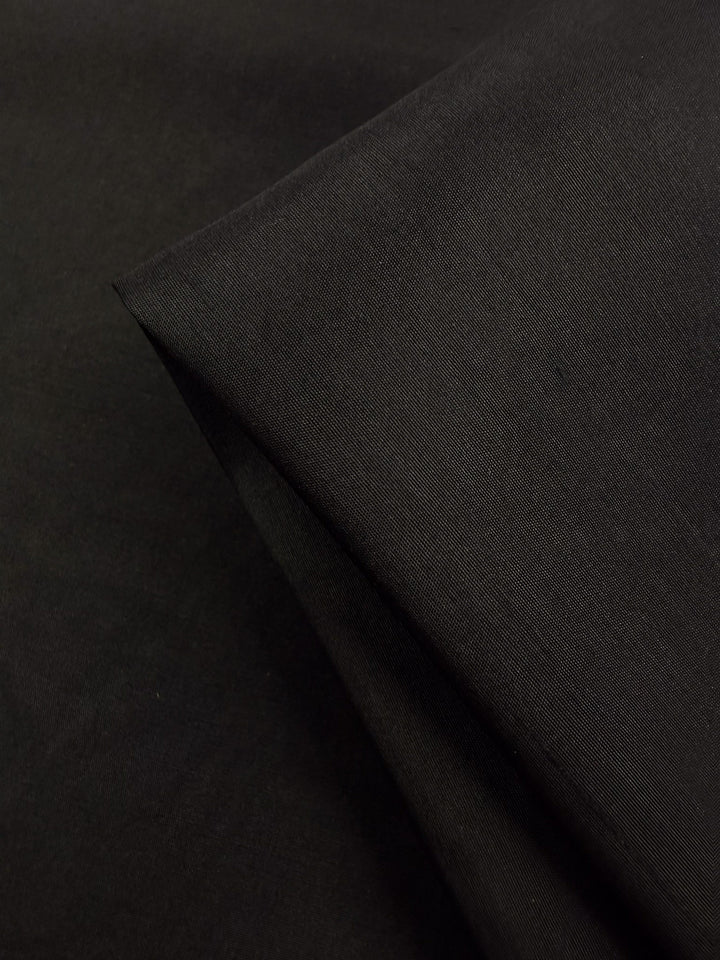 A close-up of Pure Silk Faille - Black - 115cm by Super Cheap Fabrics, with a folded section highlighting its smooth, slightly textured surface.