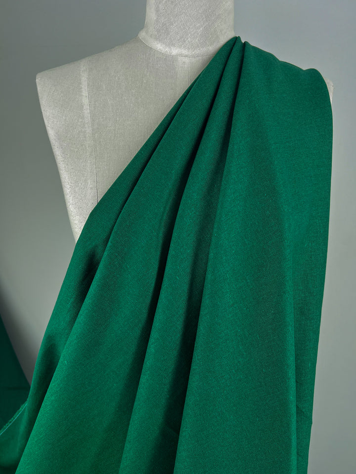 A mannequin adorned with Premium Linen Cotton - Aventurine - 140cm from Super Cheap Fabrics stands against a neutral background. The fabric cascades elegantly over one shoulder, highlighting its rich color and smooth texture.