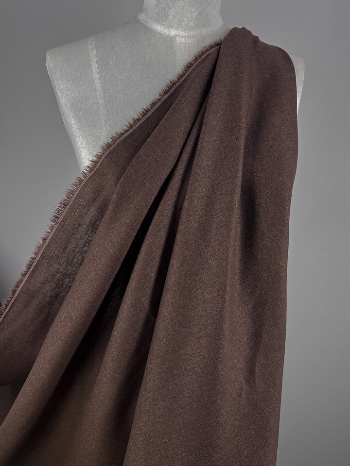 The "Premium Linen Cotton - Rocky Road - 140cm" by Super Cheap Fabrics is showcased draped over a torso mannequin against a gray backdrop. This lightweight fabric, in its elegant Rocky Road shade, features slightly frayed edges that accentuate its texture and graceful drape.