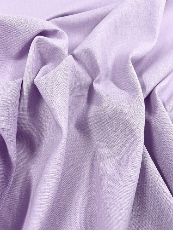 A close-up of crumpled Premium Linen Cotton by Super Cheap Fabrics showcases its lightweight, soft texture in the Orchid Bouquet hue. The gently gathered fabric forms folds and shadows, accentuating its sheen.