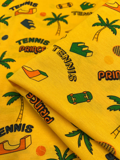 A vibrant yellow jersey from Super Cheap Fabrics showcases playful patterns adorned with palm trees, tennis rackets, and skateboards. This medium-weight fabric embodies a fun, sporty theme featuring the bold words "Tennis Prince," along with its two-way stretch for comfort and flexibility.