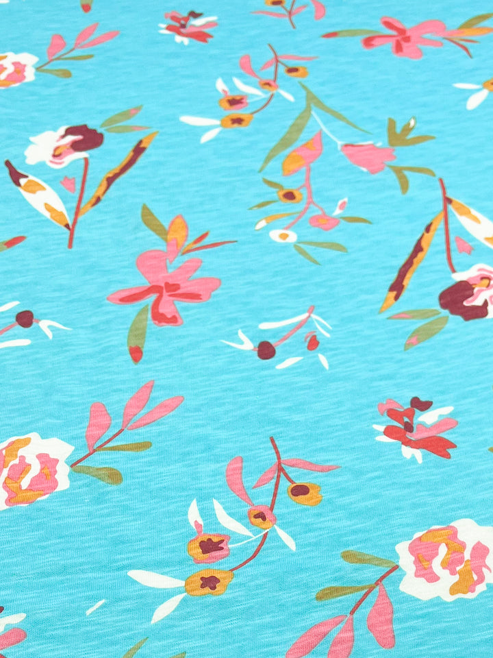 The Printed Jersey - Evelyn from Super Cheap Fabrics features a vibrant floral pattern on a blue background, crafted from medium-weight fabric. It showcases pink, yellow, and white flowers with green and red leaves. Perfect for childrenswear, this fabric adds a playful touch to any wardrobe.