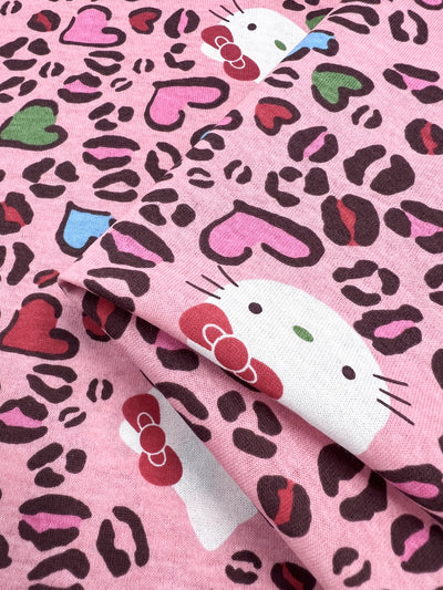 A close-up of the "Printed Jersey - Hello - 150cm" from Super Cheap Fabrics reveals a delightful pink cotton jersey, embellished with cartoon cat faces sporting bows, set against a playful leopard print backdrop and adorned with colorful hearts in shades of red, pink, blue, and green. This lightweight printed jersey fabric masterfully combines whimsy with vibrant charm.