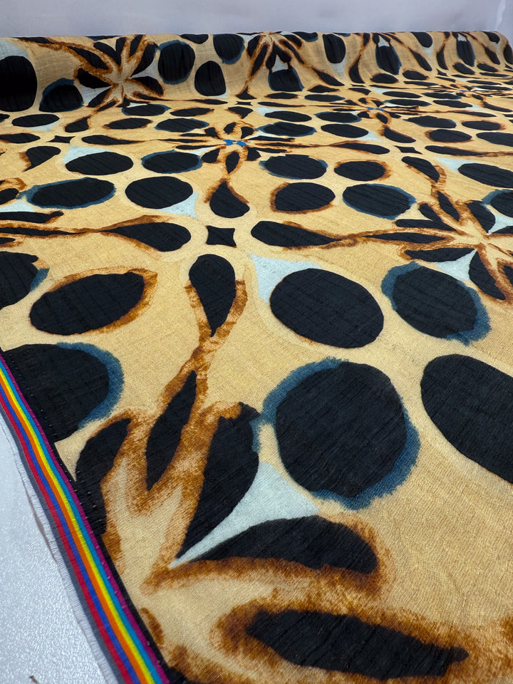 Super Cheap Fabrics' Textured Designer Cotton - Terra Dot (145cm) is a lightweight patterned cotton featuring large black circles, brown and grey abstract shapes, and a rainbow-striped edge, displayed on a flat surface.