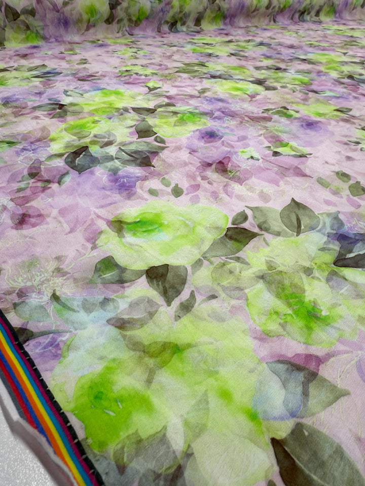 A close-up of Super Cheap Fabrics' Designer Cotton - Lime Smoke (145cm), a lightweight cotton with green, purple, and light brown floral patterns and a multicolored striped edge, perfect for quilting projects.
