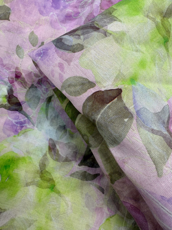 Close-up of "Designer Cotton - Lime Smoke - 145cm" by Super Cheap Fabrics—sheer, lightweight cotton with a watercolor floral pattern in pastel green, purple, and brown—perfect for quilting or adding style to your projects.