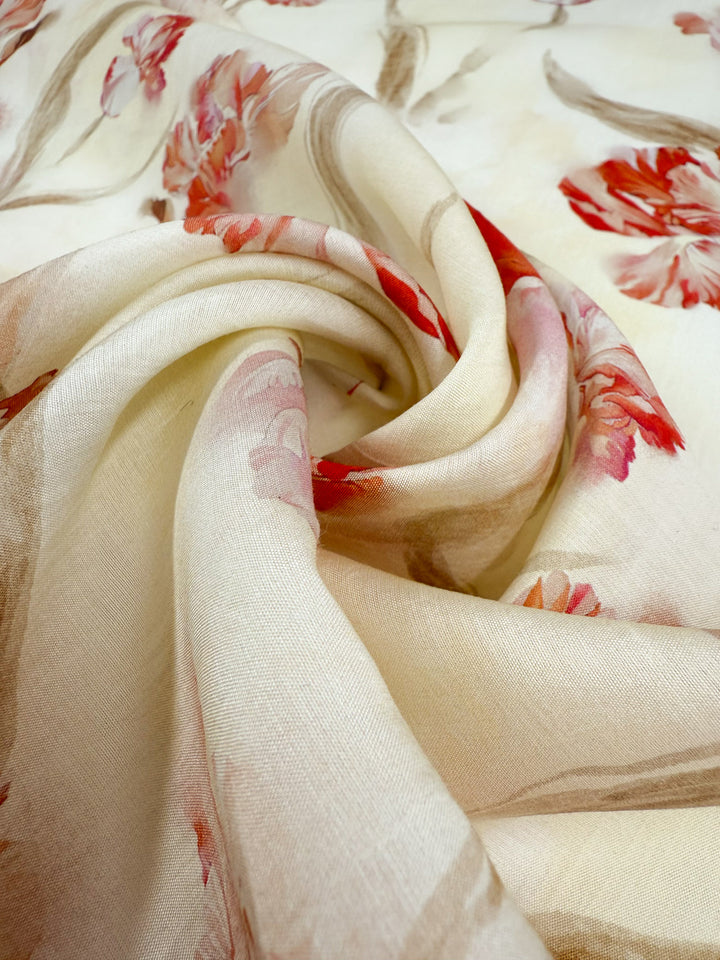 A close-up of Super Cheap Fabrics’ Designer Cotton - Painted Petal (145cm), a lightweight, cream-colored fabric with swirling folds and a delicate red, pink, and beige floral pattern. The material looks light and slightly translucent.