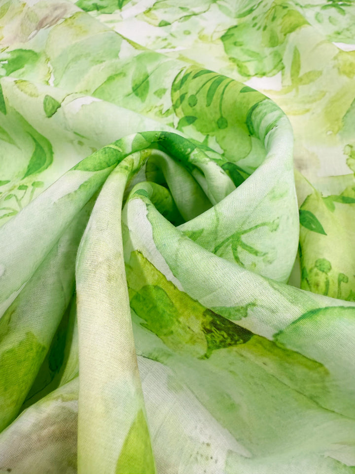 Close-up of Super Cheap Fabrics' Designer Cotton - Garden Fade (145cm), featuring a green and white watercolor floral print on lightweight cotton with gentle folds—ideal for luxury sewing projects.