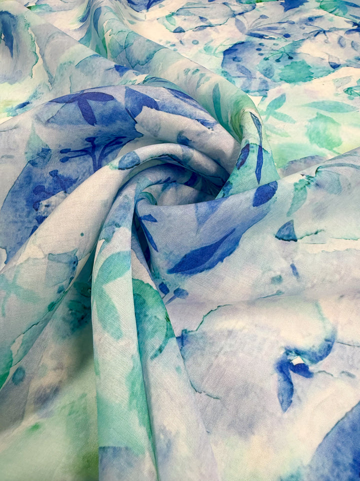 A close-up of Super Cheap Fabrics' Designer Cotton – Oceans (145cm), showcasing lightweight cotton with a swirling watercolor floral print in blue, teal, and green—ideal for sewing projects.