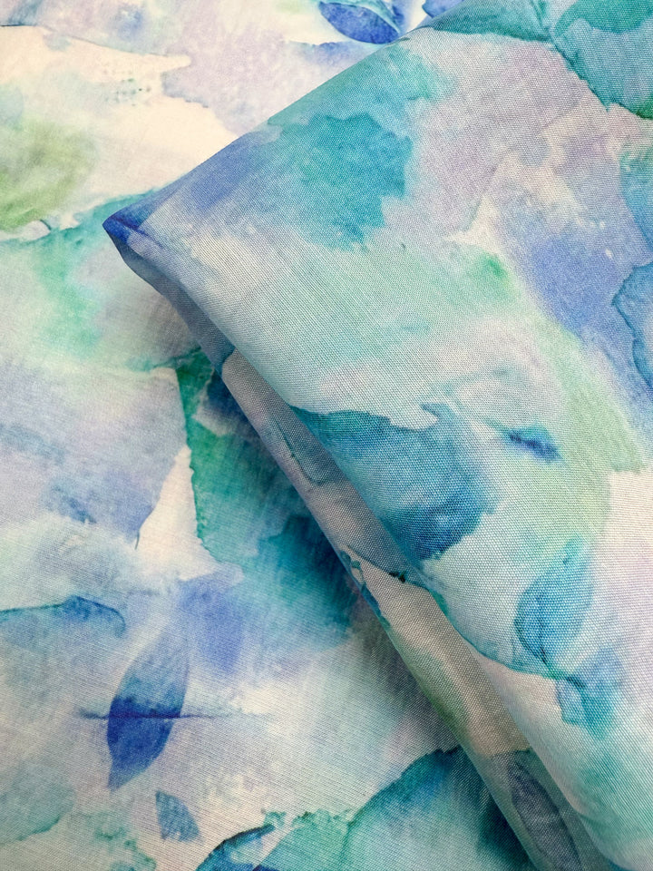 Close-up of Super Cheap Fabrics’ Designer Cotton - Oceans (145cm), featuring a lightweight, soft cotton with a soothing watercolor pattern in blue, teal, and light green—ideal for textured sewing projects needing gentle color.